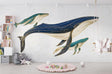 Marine life wallpaper featuring whales in navy and gold, displayed in a modern nursery with soft lighting