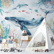 Ocean whale wallpaper mural in cozy nursery with soft lighting and wooden furniture