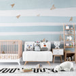 Blue and white striped nursery wallpaper with gold planes in a bright modern nursery with white furniture