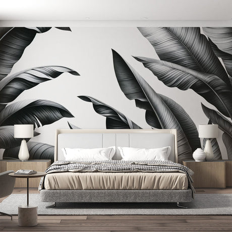Black and white tropical leaf mural wallpaper shown in a bright modern living room with minimal furniture