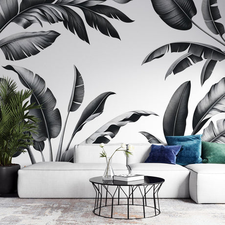 Black and white tropical leaf mural wallpaper creating a stunning focal point in a modern living room with minimalist furniture