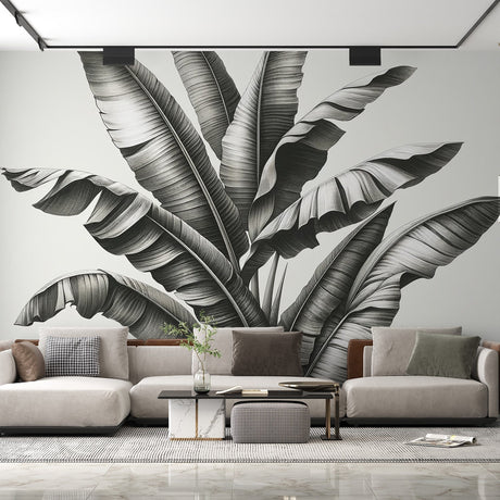 Black and white tropical leaf mural wallpaper creating depth in a modern living room with clean furniture and natural light