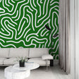 Modern green labyrinth abstract wallpaper creating depth in a bright, minimalist living room with white furniture