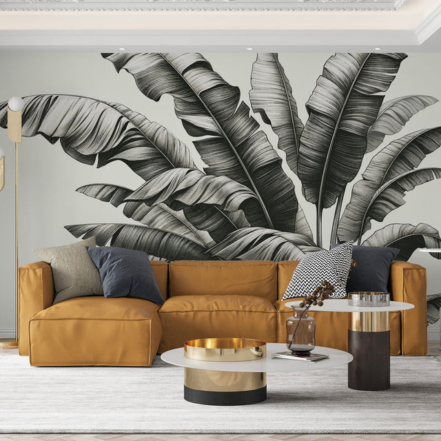 Black and white banana leaf wallpaper mural creating a striking accent wall in a modern living room with minimal furniture