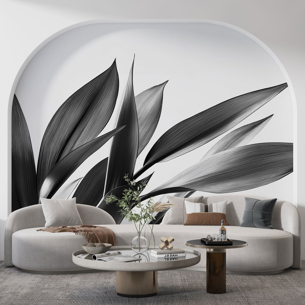 Black and white botanical leaf mural wallpaper styled in a modern living room with minimal furniture and natural light