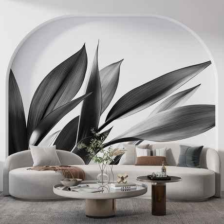Black and white botanical leaf mural wallpaper styled in a modern living room with minimal furniture and natural light