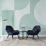 Modern geometric wallpaper in sage green tones shown in a bright living room setting with minimal furniture