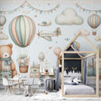 Hot air balloon nursery wallpaper in soft pastels shown in a bright children's bedroom with white furniture and natural light