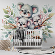 Koala family wallpaper mural in a bright nursery setting, showing three cute koalas among watercolor leaves