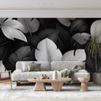 Modern living room with black and white Monstera leaf wallpaper creating a bold statement wall behind grey sofa