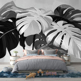 Black and white Monstera leaf wallpaper creating a striking focal point in a modern living room with minimalist furniture