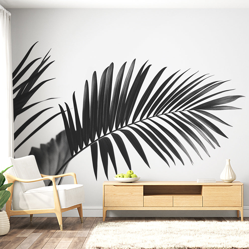 Black and white palm leaf mural wallpaper creating a bold statement in a bright modern living room with minimal furniture