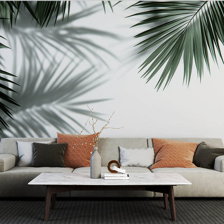 Tropical palm leaves wallpaper creating elegant shadows in a modern living room with white walls and minimal furniture