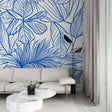 Blue tropical line art wallpaper in a bright modern living room, showing the pattern's clean aesthetic and room-expanding effect