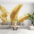 Golden banana leaf wallpaper mural creating a luxury tropical feel in a modern living room with white sofa and natural decor